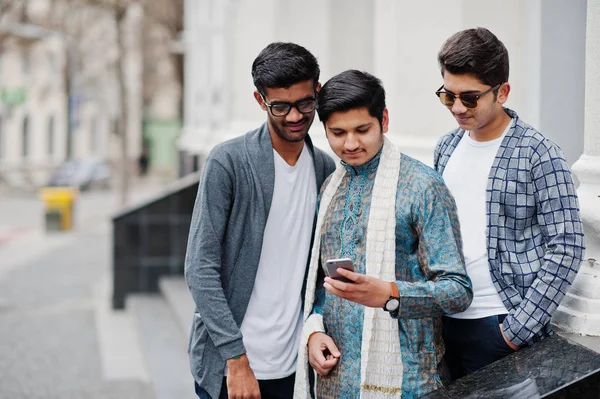 Group of three south asian indian mans in traditional and casual wear looking at mobile phone.