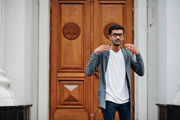 Stylish indian man at glasses wear casual posed outdoor against door of building.