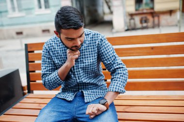 Şık Hint sakal modeli adam rahat kıyafetler içinde Hindistan Street bankta oturmuş ve onun saatler seyir açık, yarattığı.