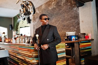 Zarif siyah ceket ve güneş gözlüğü, holding retro baston baston şişesi veya altın elmas topu saplı tippling kamışı olarak şık Afro-Amerikan beyefendi. Zengin moda afro adam.