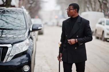 Zarif siyah ceket, holding retro baston baston şişesi veya altın elmas topu saplı tippling kamışı olarak şık Afro-Amerikan beyefendi. Zengin moda afro insan iş suv araba karşı.