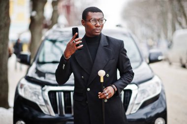 Zarif siyah ceket, holding retro baston baston şişesi veya tippling kamışı olarak şık Afro-Amerikan beyefendi. Zengin moda afro adama karşı iş suv araba üstünde hareket eden telefon konuşma.