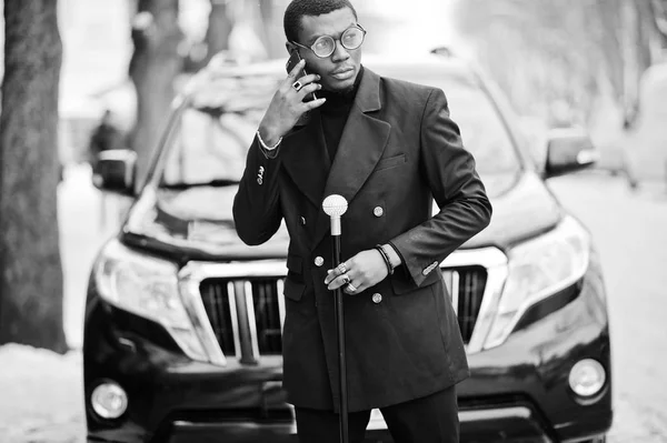 エレガントな黒のジャケット 持株レトロなステッキ杖フラスコまたは Tippling 杖としてスタイリッシュなアフリカ系アメリカ人紳士 携帯電話で話すビジネス Suv 車に対する豊富なファッショナブルなアフロ男 — ストック写真
