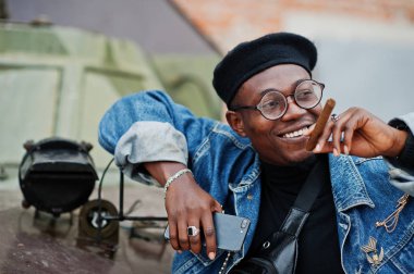 Ben senin kaptanınım. Btr askeri zırhlı araç karşı Afro-Amerikan erkek kot ceket, bere ve gözlük, puro ile poz verdi.