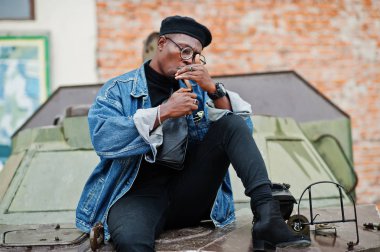 Afro-Amerikan erkek kot ceket, bere ve gözlük, bir puro ışıklar ve btr askeri zırhlı araç karşı yöneltilen.