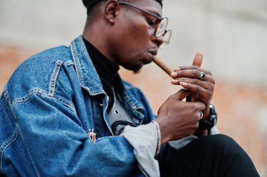 Kot ceket, bere ve gözlük, Afrikalı-Amerikalı adam ışıklar bir puro.