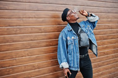 Afrika kökenli Amerikalı adam kahverengi çekim zemin üzerine puro sigara kot ceket, bere ve gözlük,.