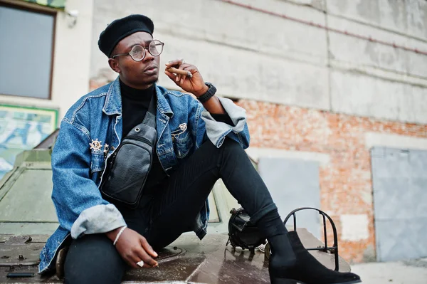 African american man in jeans jacket, beret and eyeglasses, smoking cigar and posed against btr military armored vehicle.