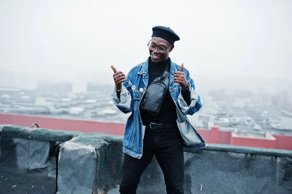 African american man in jeans jacket, beret and eyeglasses posed on abandoned roof.