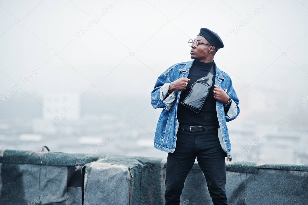 African american man in jeans jacket, beret and eyeglasses posed on abandoned roof.