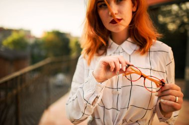 Gözlük redhaired kadın, beyaz bluz tutan fotoğrafını ekrana kapatın.