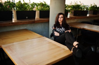 Bir barda deri ceketli genç kıvırcık kadın bacaklarını masanın üstüne koy..