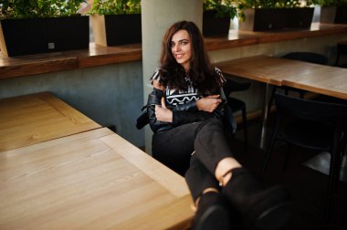 Bir barda deri ceketli genç kıvırcık kadın bacaklarını masanın üstüne koy..