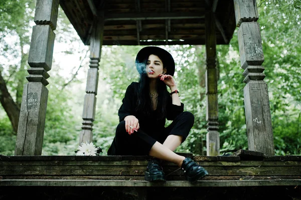 Sensual smoker girl all in black, red lips and hat. Goth dramatic woman smoking thin cigarette.