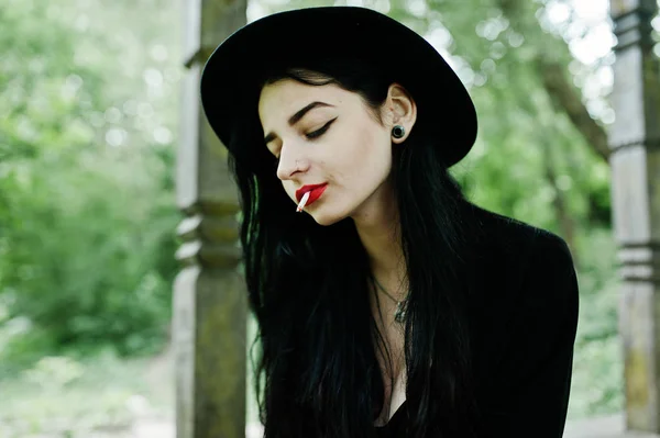 Sensual smoker girl all in black, red lips and hat. Goth dramatic woman smoking thin cigarette.