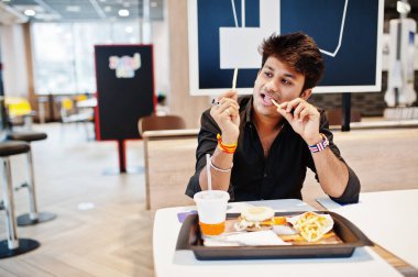Fast food café'de oturan ve patates kızartması, yeme komik ve şık Hintli adam dilini göster.