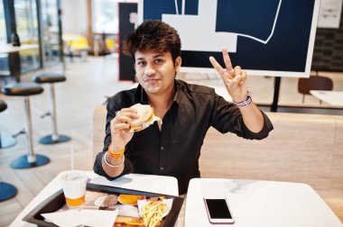 Fast food café'de oturan ve hamburger ve jest barış üye el yemek şık Hintli.
