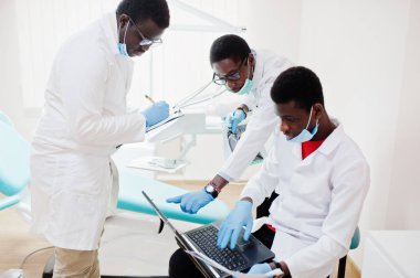 Diş Kliniği meslektaşları ile tartışırken laptop ile çalışan üç Afro-Amerikan erkek doktor. 