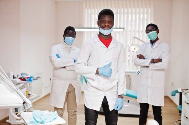 Three african american male doctor with crossed arms in dental clinic. Show thumb up. clipart