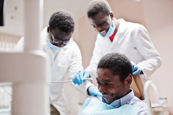 African american man patient in dental chair. Dentist office and doctor practice concept. Laughter at the workplace. Drilling patient's teeth in clinic.