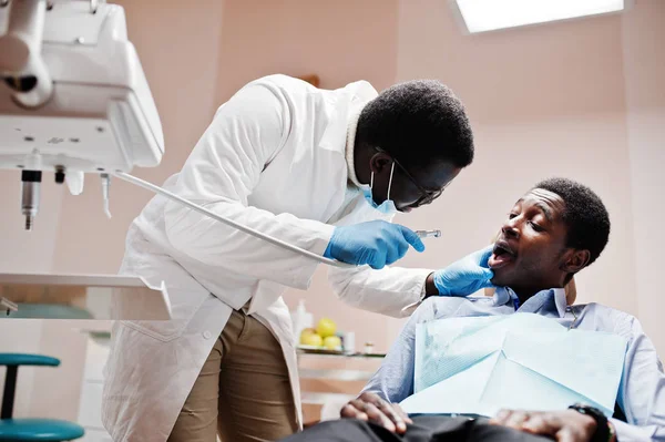 African american man patient in dental chair. Dentist office and doctor practice concept. Professional dentist helping his patient at dentistry medical. Drilling patient\'s teeth in clinic.