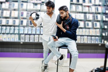 İki Hintliler müşteri alıcı earphones ve kablosuz hoparlör dinleme müzik ile cep telefonu mağazasında mans. Güney Asya halkları ve teknolojileri kavramı. Cep Telefonu Dükkanı.