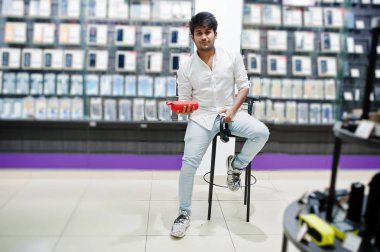 Hintli müşteri alıcı cep telefonu Store kablosuz kulaklık ve hoparlör sandalyede oturuyor. Güney Asya halkları ve teknolojileri kavramı. Cep Telefonu Dükkanı.