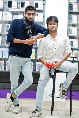 İki Hintliler müşteri alıcı earphones ve kablosuz hoparlör dinleme müzik ile cep telefonu mağazasında mans. Güney Asya halkları ve teknolojileri kavramı. Cep Telefonu Dükkanı.