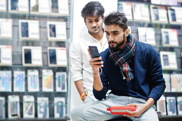Two indians mans customer buyer at mobile phone store with earphones and wireless speaker listening music. South asian peoples and technologies concept. Cellphone shop.