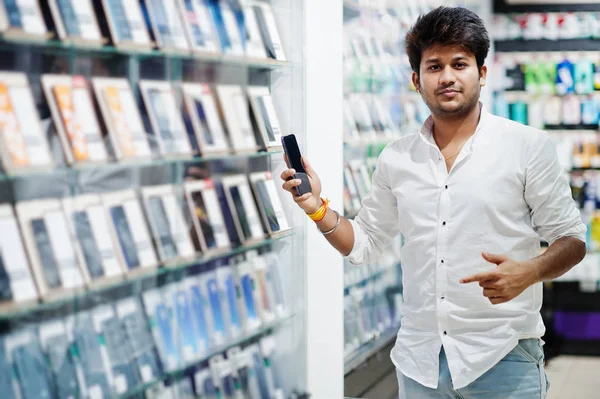 Indian man customer buyer at mobile phone store choose his new smartphone. South asian peoples and technologies concept. Cellphone shop.