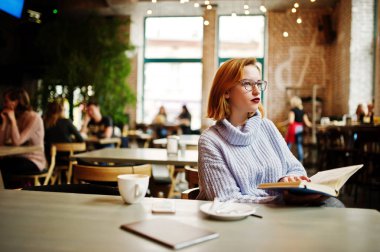 Neşeli genç güzel redhaired kadın çalışma evinde Kafe üzerinde oturan ve kahve içme gözlük.