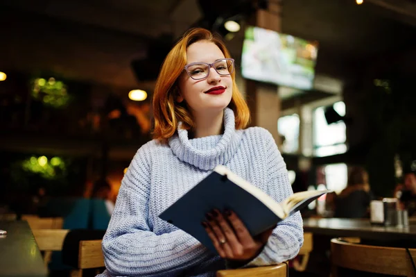 在咖啡馆的工作场所 穿着眼镜的年轻美丽的红头发的女人坐在她的工作场所 在笔记本上读着一些东西 — 图库照片