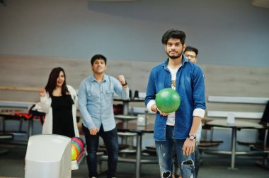 Kot gömlek ayakta eller üzerinde topu ile bowling salonu, Güney Asya adam. Adam bir atmak için hazırlanıyor. Arkadaşları ona destek.