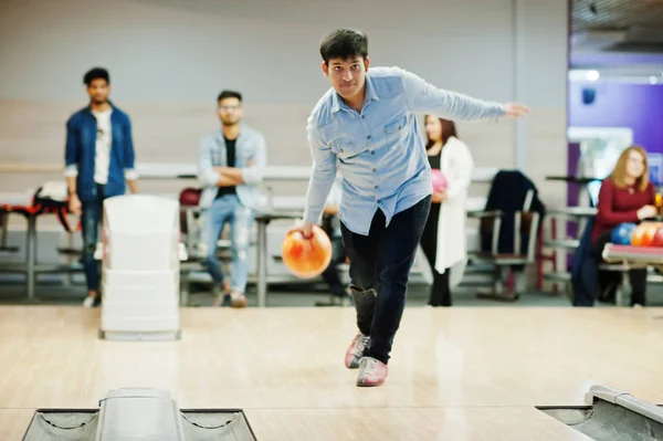 South asian man in jeans shirt standing at bowling alley and throw ball.
