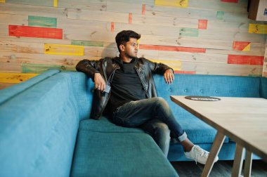 Rahat ve şık genç Asyalı erkek giyimi cellphone ile eldeki kafede oturan deri ceket.