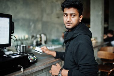 Rahat ve şık genç Asyalı adam pos terminal üzerinde kredi kartıyla ödeme bar cafe kulaklık ile.