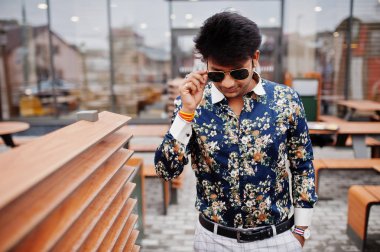 Çekici ve yakışıklı şık Hintli giymek gömlek ve modern lounge café'de iş molası Teras ayakta güneş gözlüğü.