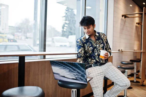 Young male indian freelancer sitting open laptop computer in fast food cafe, handsome asian man reading text message during work on net-book in comfortable coffee shop.