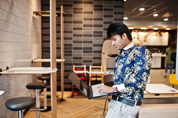 Young male indian freelancer sitting open laptop computer in fast food cafe, handsome asian man reading text message during work on net-book in comfortable coffee shop.