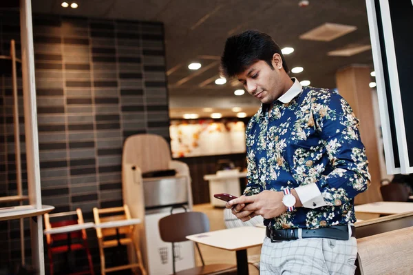 Young male indian freelancer in fast food cafe, handsome asian man reading text message during work on mobile phone in comfortable coffee shop.