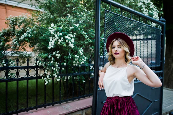 ゲートに対して屋外ポーズでスタイリッシュな赤いベルベット ベロア スカート 白のブラウス ファッショナブルで美しい金髪モデルの女の子 — ストック写真