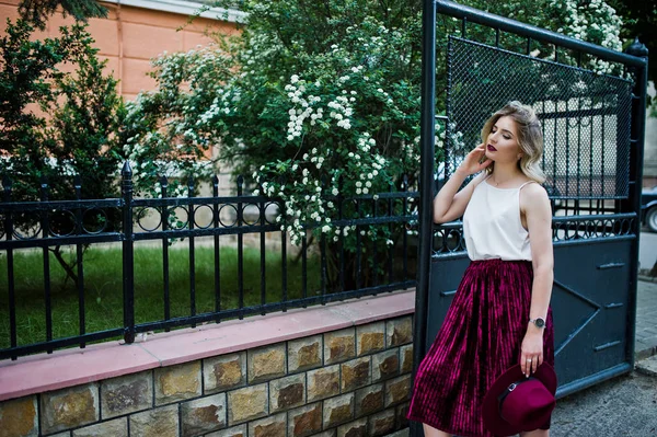 ゲートに対して屋外ポーズでスタイリッシュな赤いベルベット ベロア スカート 白のブラウス ファッショナブルで美しい金髪モデルの女の子 — ストック写真