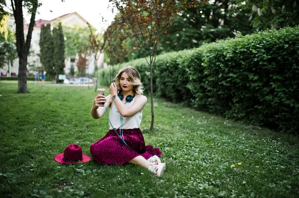 스커트 블라우스와 이어폰 공원에서 잔디에 앉아에서 그녀는 Selfie — 스톡 사진