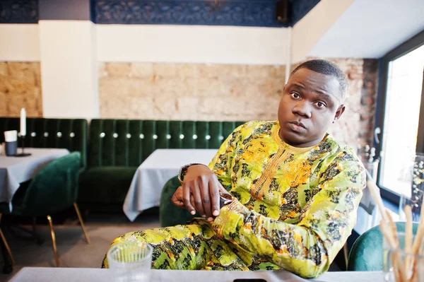 Chockad ansikte afro man i traditionella kläder sitter vid restaura — Stockfoto