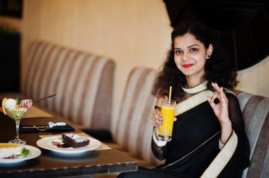 Genç Hint kadın Wear at zarif siyah Saree oturan üzerinde Restau