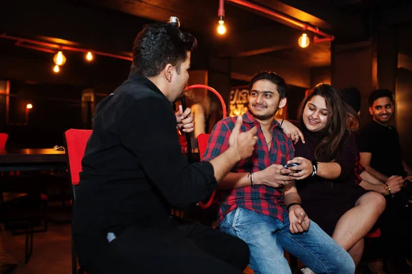 Group of indian friends sitting at lounge bar, smoke hookah and — Stock Photo, Image