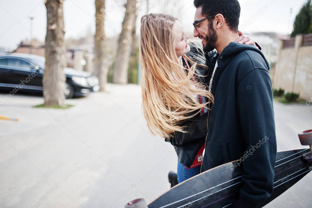 Cool multiracial couple walking together with longboard.