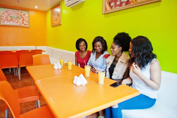 Quatro jovens africanas com sucos sentados em cores brilhantes f — Fotografia de Stock
