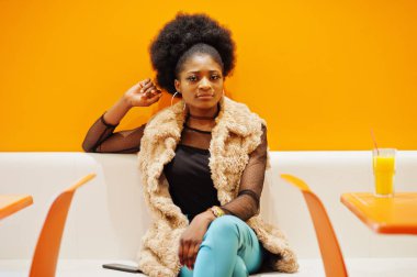 Ananas ile turuncu duvara karşı kafede oturan Afrikalı kadın