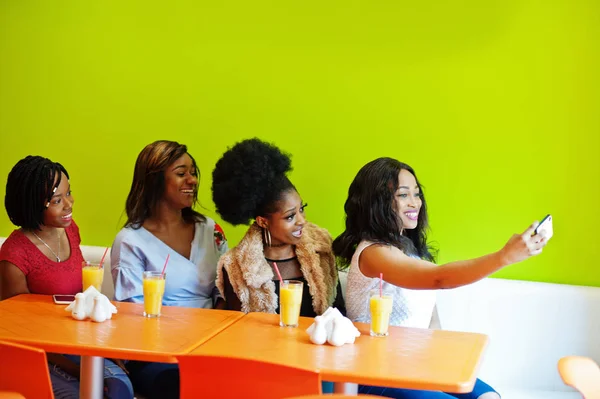 Quatro jovens africanas com sucos sentados em cores brilhantes f — Fotografia de Stock